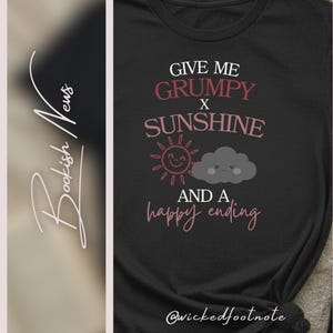 May include: Black t-shirt with the text "GIVE ME GRUMPY X SUNSHINE AND A happy ending". The design includes a smiling sun and a grumpy cloud. The text and graphics are in shades of pink and white.