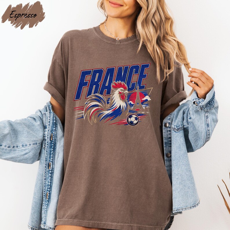 A woman wearing a brown t-shirt with a graphic of a rooster and the word "FRANCE" printed on it, along with a denim jacket.