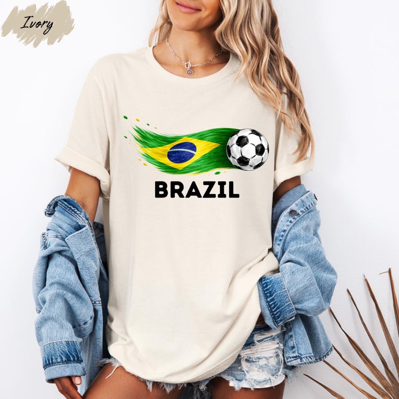 A woman wearing a white t-shirt with a graphic of the Brazilian flag and a soccer ball, along with the word "BRAZIL" printed on it. She is also wearing denim clothing and has a denim jacket on her shoulders.