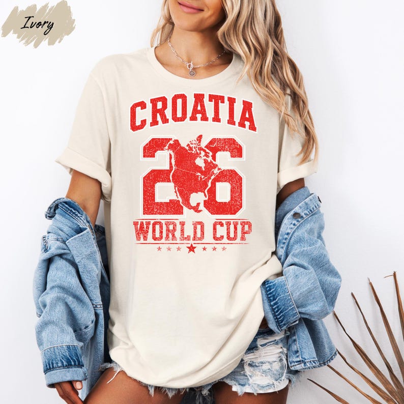A woman wearing a white t-shirt with the text "Croatia 26 World Cup" printed on it, along with a graphic of a map and stars. She is also wearing a denim jacket and denim shorts.