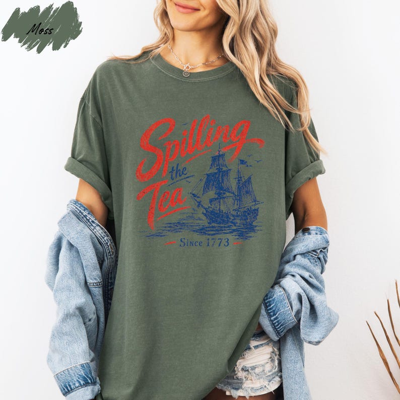 A woman wearing a green t-shirt with a graphic design of a ship and the text "Spilling the Tea Since 1773" printed on it.