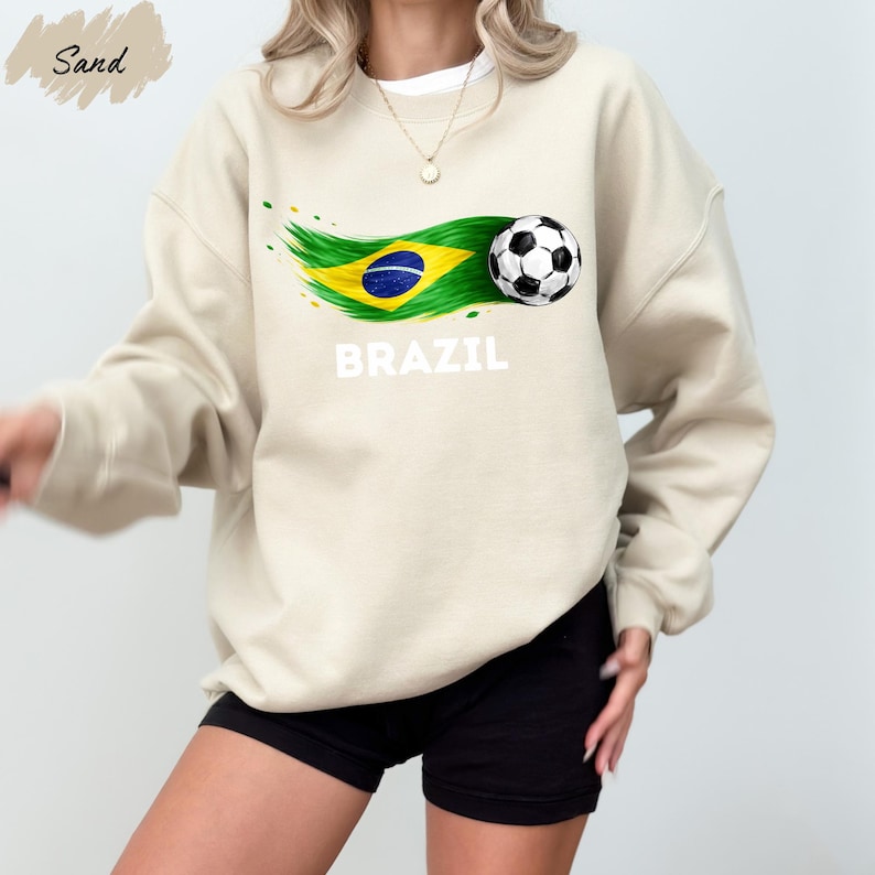 A woman wearing a beige sweatshirt with a graphic of a soccer ball and the word "BRAZIL" printed on it, along with a Brazilian flag design.