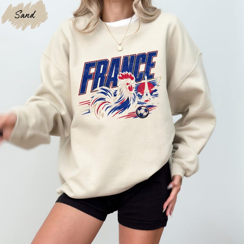A person wearing a beige sweatshirt with a graphic design featuring a rooster and the word "FRANCE" printed on it.