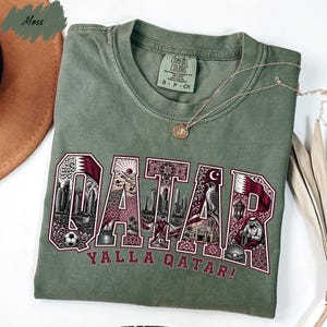 A green t-shirt with the word "QATAR" printed on it, along with various images and text related to the country of Qatar.