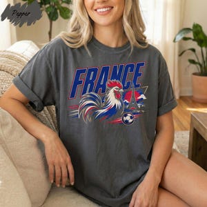A woman wearing a gray t-shirt with a graphic design of a rooster and the word "FRANCE" printed on it.