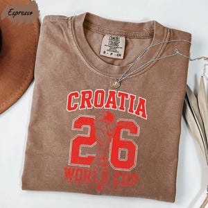 A brown t-shirt with the text "Croatia 26 WORLD CUP" printed on it, along with a number "26" and a trophy icon.