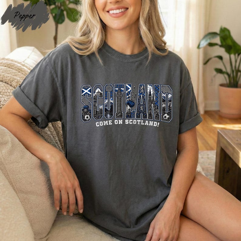 A woman wearing a grey t-shirt with the word "SCOTLAND" printed on it, sitting on a couch.