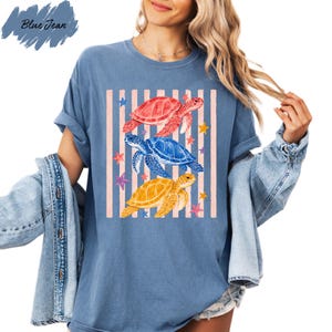 A woman wearing a blue t-shirt with a graphic design of three colorful sea turtles and stars.