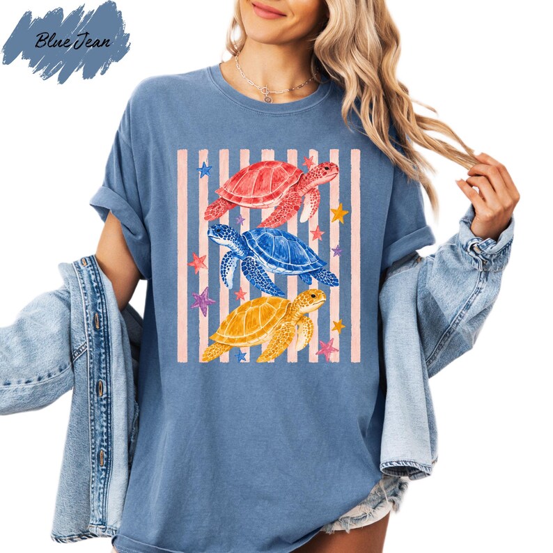 A woman wearing a blue t-shirt with a graphic design of three colorful sea turtles and stars.