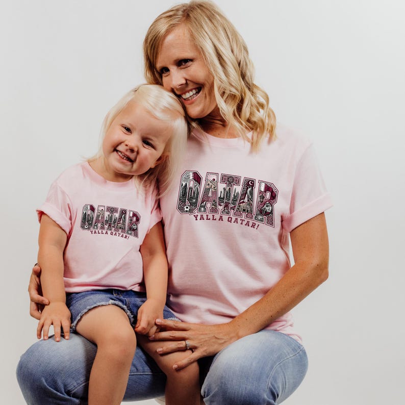 A smiling woman wearing a pink t-shirt with the word "GAMAR" and a child wearing a matching pink t-shirt are posing together.