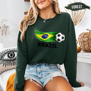 A woman wearing a green sweatshirt with a graphic of the Brazilian flag and a soccer ball, along with the word "BRAZIL" printed on it.
