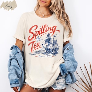 A woman wearing a white t-shirt with a graphic design of a ship and the text "Spilling the Tea Since 1773" printed on it.