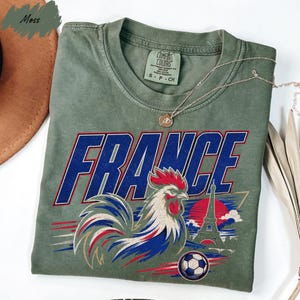 a green t-shirt with a graphic design of a rooster and a soccer ball, along with the word "FRANCE" written on it.