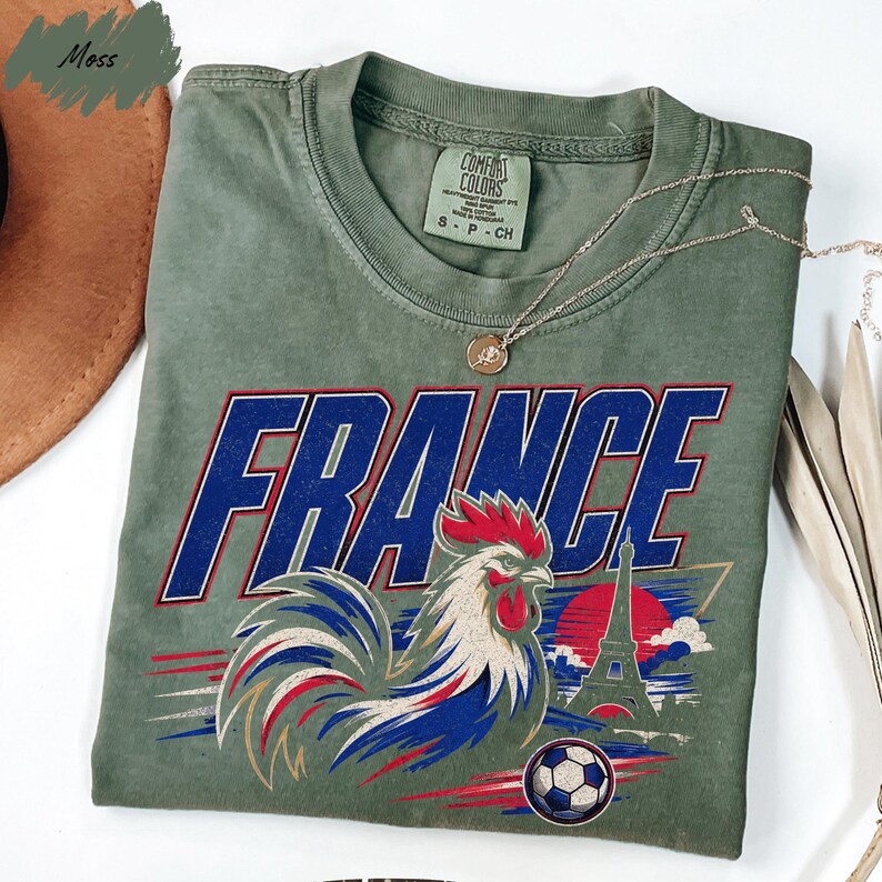 a green t-shirt with a graphic design of a rooster and a soccer ball, along with the word "FRANCE" written on it.