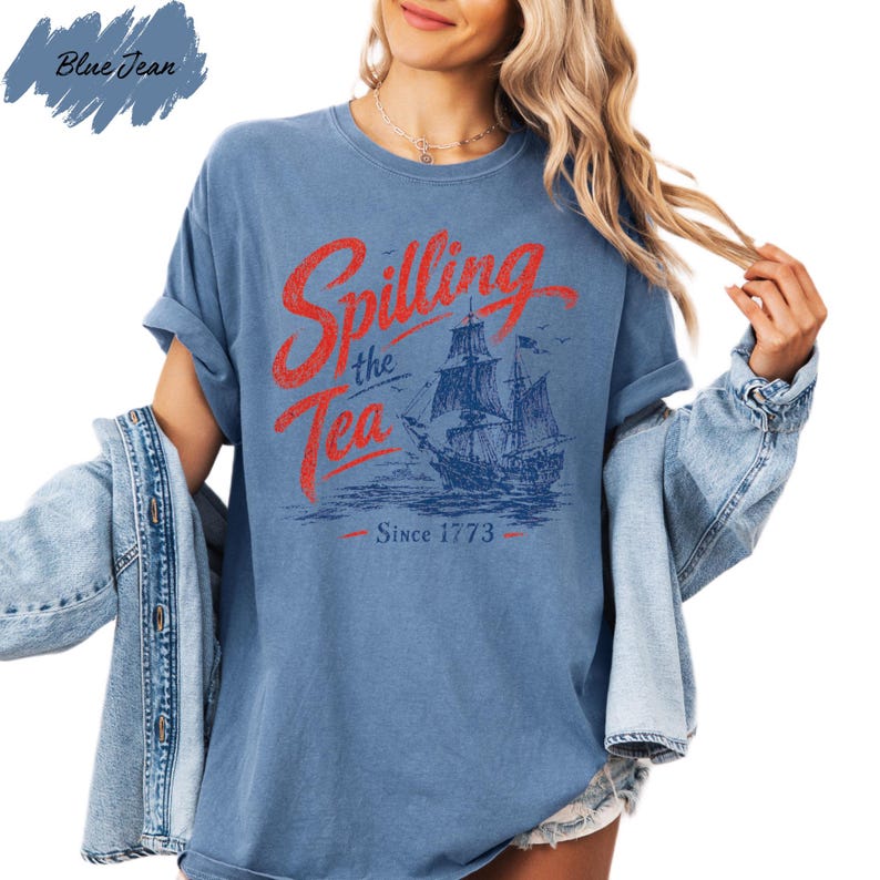 A woman wearing a blue t-shirt with a graphic design of a ship and the text "Spilling the Tea Since 1773" printed on it.