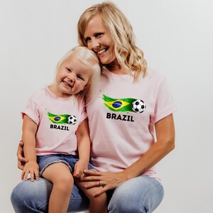 A smiling woman and a young girl wearing matching pink t-shirts with the word "BRAZIL" printed on them.