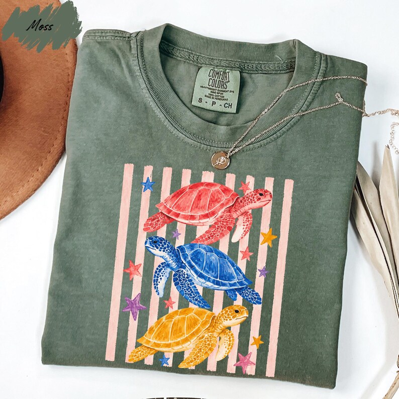 a green t-shirt with a colorful graphic design featuring three turtles and stars on a striped background.