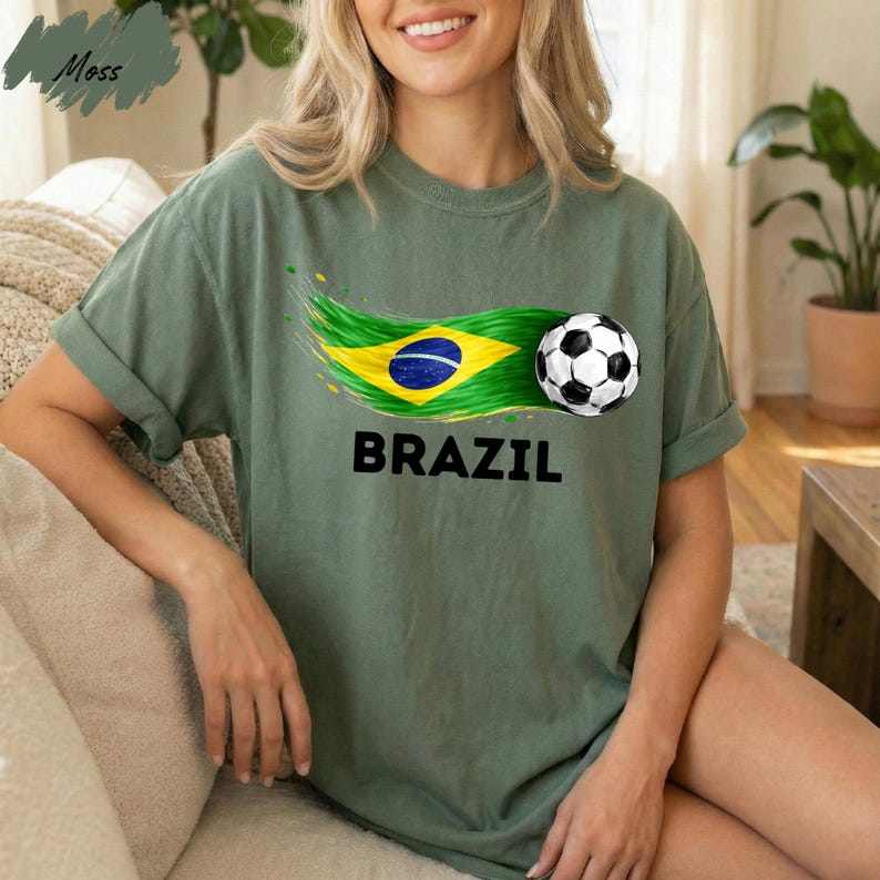 A woman wearing a green t-shirt with a graphic of the Brazilian flag and a soccer ball printed on it, sitting on a couch.