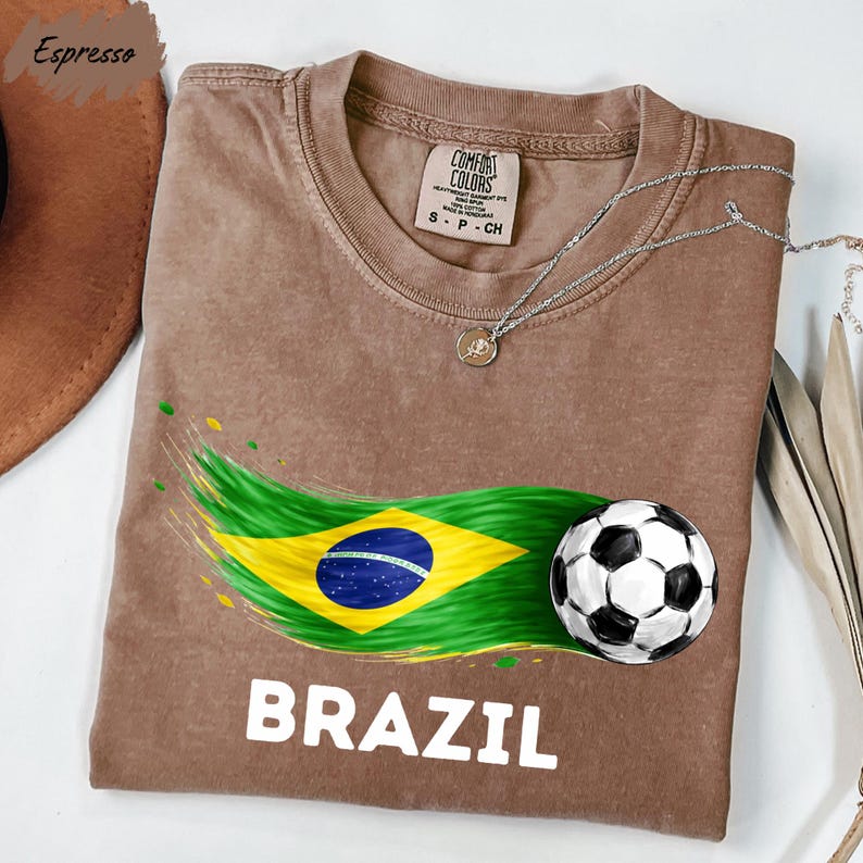 a brown t-shirt with a graphic design depicting the Brazilian flag and a soccer ball, along with the word "BRAZIL" printed on it.