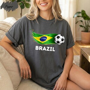 A woman wearing a gray t-shirt with the word "BRAZIL" printed on it, along with a graphic of a soccer ball and the Brazilian flag.