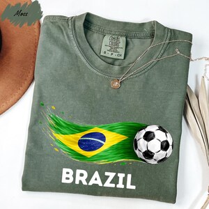 a green t-shirt with a graphic design of the Brazilian flag and a soccer ball, along with the word "BRAZIL" printed on it.