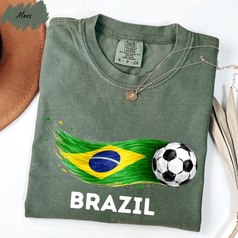 a green t-shirt with a graphic design of the Brazilian flag and a soccer ball, along with the word "BRAZIL" printed on it.