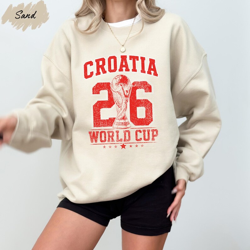 A person wearing a beige sweatshirt with a red and white graphic that says "Croatia 26 WORLD CUP".