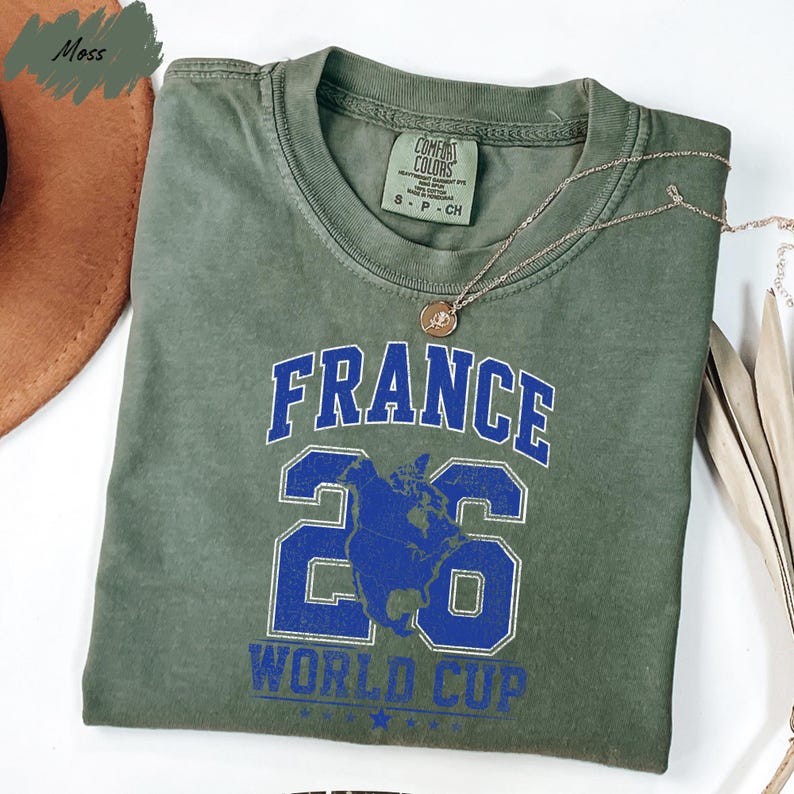 A green t-shirt with the text "FRANCE 26 WORLD CUP" printed on it, along with a number "26" and a graphic of a globe.