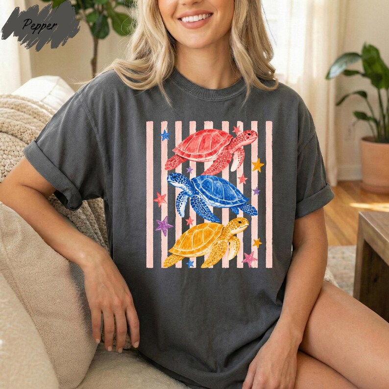 A woman wearing a gray t-shirt with a colorful graphic design of three sea turtles and stars on it.