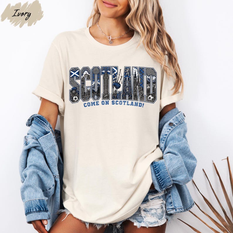 A woman wearing a white t-shirt with the word "SCOTLAND" printed on it, along with the text "COME ON SCOTLAND!" printed below. She is also wearing denim clothing, including a denim jacket and denim shorts.