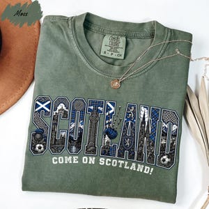 A green t-shirt with the word "SCOTLAND" printed on it, along with various Scottish-themed graphics and text.