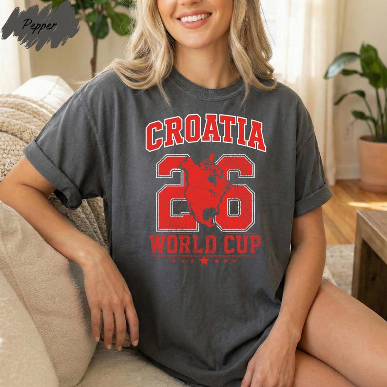 A smiling woman wearing a gray t-shirt with the text "Croatia 26 World Cup" printed on it.