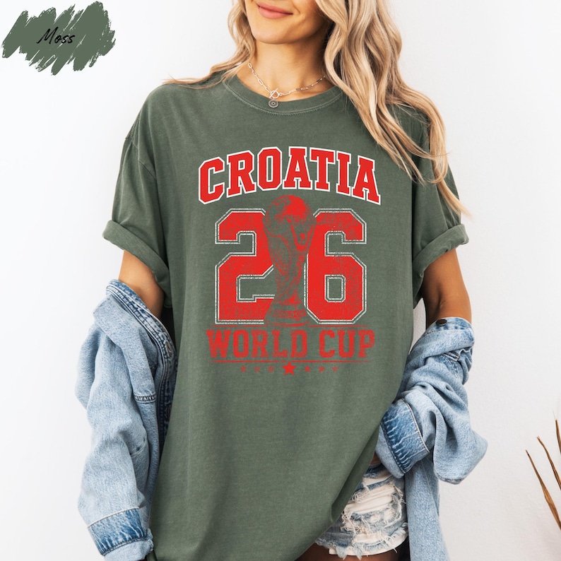 A woman wearing a green t-shirt with the text "Croatia 26 World Cup" printed on it, standing against a white background.