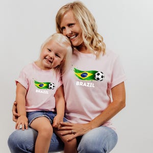 A smiling woman and a young girl wearing matching pink t-shirts with the word "BRAZIL" printed on them.