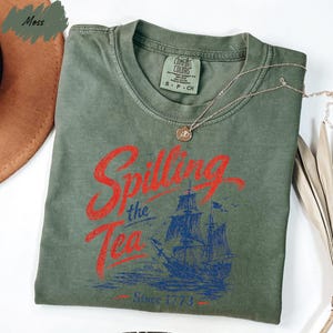 a green t-shirt with a graphic design featuring a ship and the text "Spilling the Tea Since 1773" printed on it.