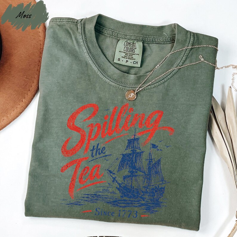 a green t-shirt with a graphic design featuring a ship and the text "Spilling the Tea Since 1773" printed on it.