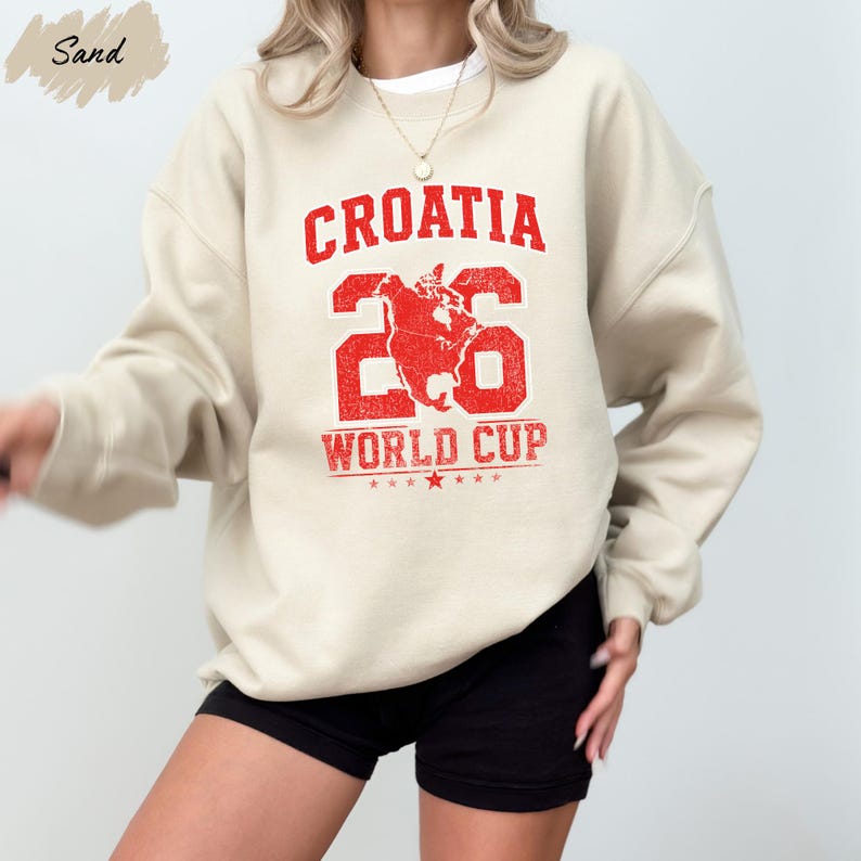 A person wearing a cream-colored sweatshirt with a red graphic and text printed on it, along with black shorts.