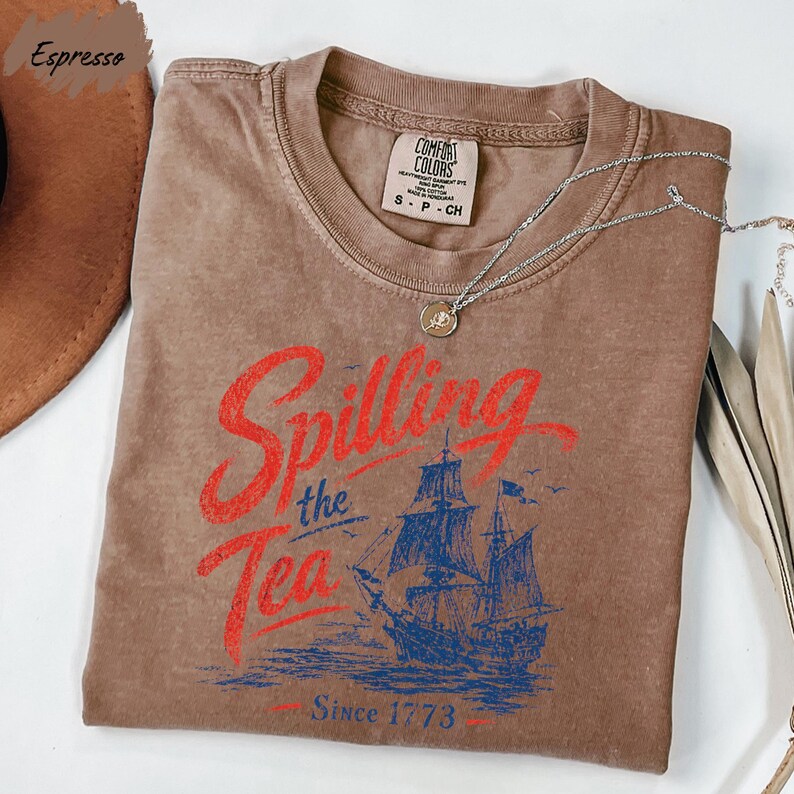 a brown t-shirt with a graphic design featuring a ship and the text "Spilling the Tea Since 1773".