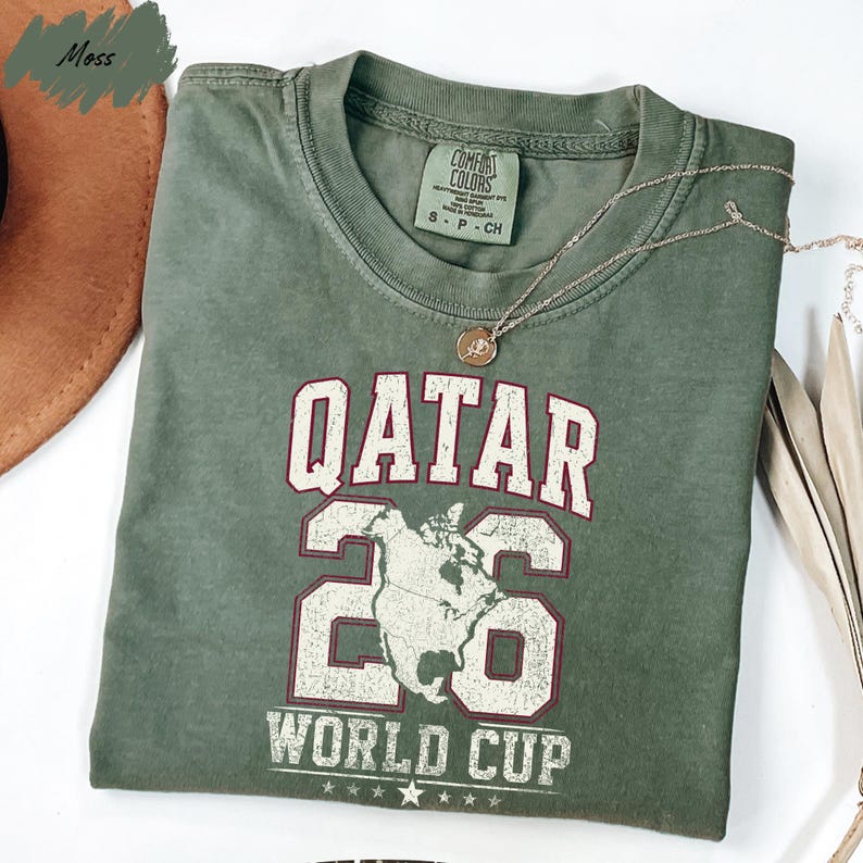 A green t-shirt with the text "QATAR 26 WORLD CUP" printed on it, along with a map of the world.