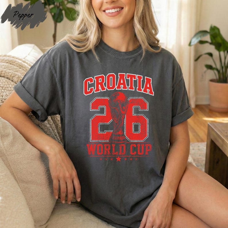 A woman wearing a grey t-shirt with the text "Croatia 26 WORLD CUP" printed on it, sitting on a couch.