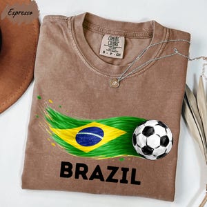 a brown t-shirt with a graphic design depicting the Brazilian flag and a soccer ball, along with the word "BRAZIL" printed on it.