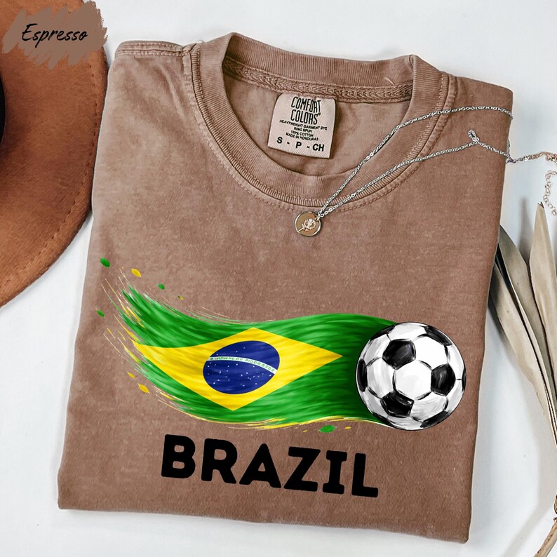 a brown t-shirt with a graphic design depicting the Brazilian flag and a soccer ball, along with the word "BRAZIL" printed on it.