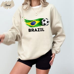 A woman wearing a white sweatshirt with a graphic of a soccer ball and the word "BRAZIL" printed on it, along with a Brazilian flag design.
