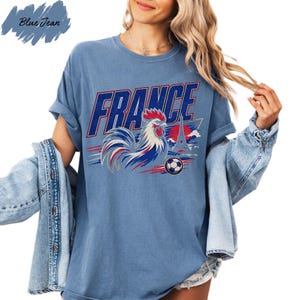 A woman wearing a blue t-shirt with a graphic of a rooster and the word "FRANCE" printed on it, along with a denim jacket.