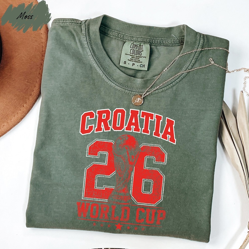A green t-shirt with red text and numbers printed on it, along with a necklace and a brown hat.
