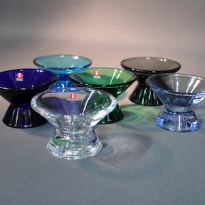 Peut inclure: Ensemble de six bols en verre colorés, bleus, verts et transparents. Chaque bol a un dessus large et peu profond et une base évasée. Les bols sont disposés sur une surface grise, mettant en valeur leurs couleurs et leur transparence. Mesures en centimètres.