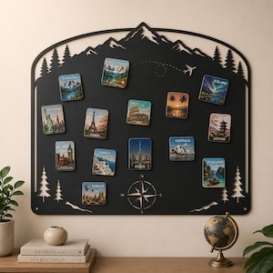 May include: A black metal wall map board featuring a mountain and pine tree silhouette frame. It includes a compass rose and a dashed flight path with a small airplane. Twelve square magnets display travel destinations: Canada, Switzerland, Iceland, New York, Paris, Italy, Bali, Japan, London, Greece, Dubai, Australia, and Thailand.