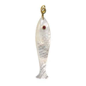 Könnte beinhalten: Ein perlmuttfarbener Fischanhänger mit goldfarbener Öse und rotem Edelsteinauge. Der Fisch ist mit Schuppen- und Flossendetails geschnitzt. Der Anhänger ist etwa 7,6 cm lang.