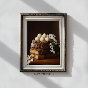 May include: A framed still life print featuring a woven basket filled with six eggs, resting atop two antique books. White flowers surround the basket and books. The print is in a dark wooden frame.