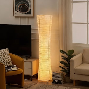 May include: A tall, cylindrical floor lamp with a textured, off-white shade. The lamp is illuminated, casting a warm glow. The lamp is a decorative lighting fixture, suitable for a living room or bedroom.